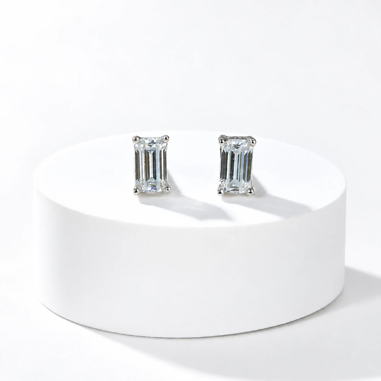 Emerald-cut diamond studs on a white plinth, background retouched
